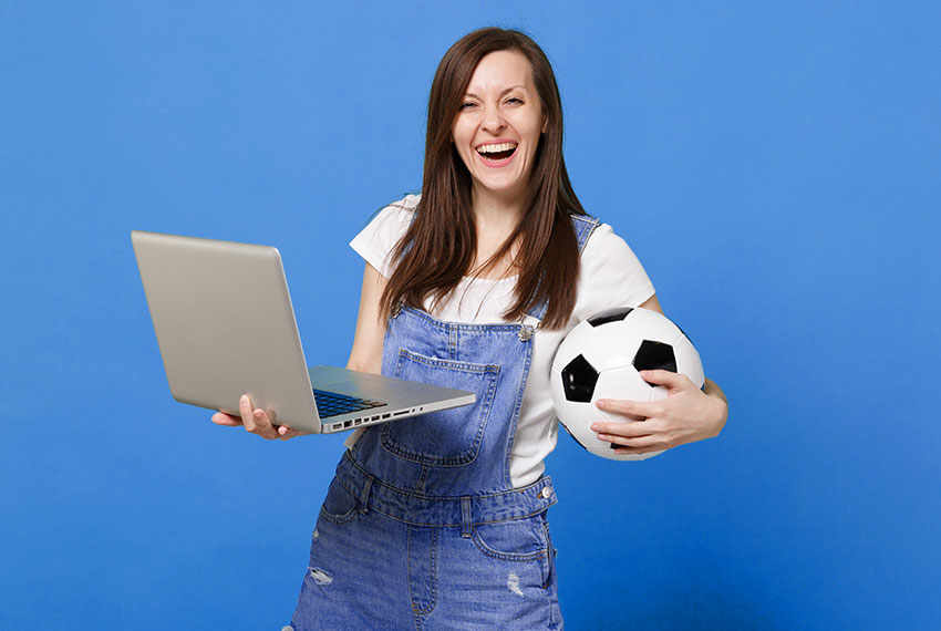 Mulher assistindo futebol pelo notebook com bola de futebol nas mãos